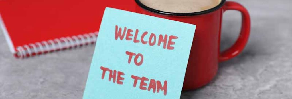 Sticky note with phrase Welcome To The Team, coffee and notebook on grey table, closeup